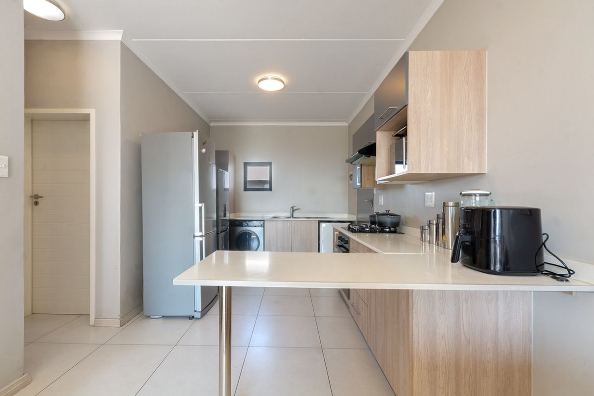 Modern kitchen featuring light wood-finish cabinetry, stone countertops, a breakfast bar, and integrated hob with extractor fan, set against neutral tiled flooring.