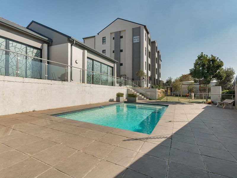 Communal swimming pool area featuring a paved deck, glass balustrades, and secure perimeter fencing within the apartment complex.