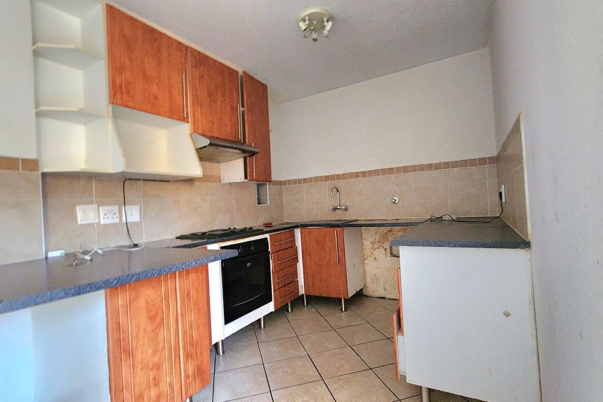 A dated kitchen featuring laminate cabinetry, built-in oven, gas hob, and tiled finishes, currently requiring maintenance and cosmetic updates.