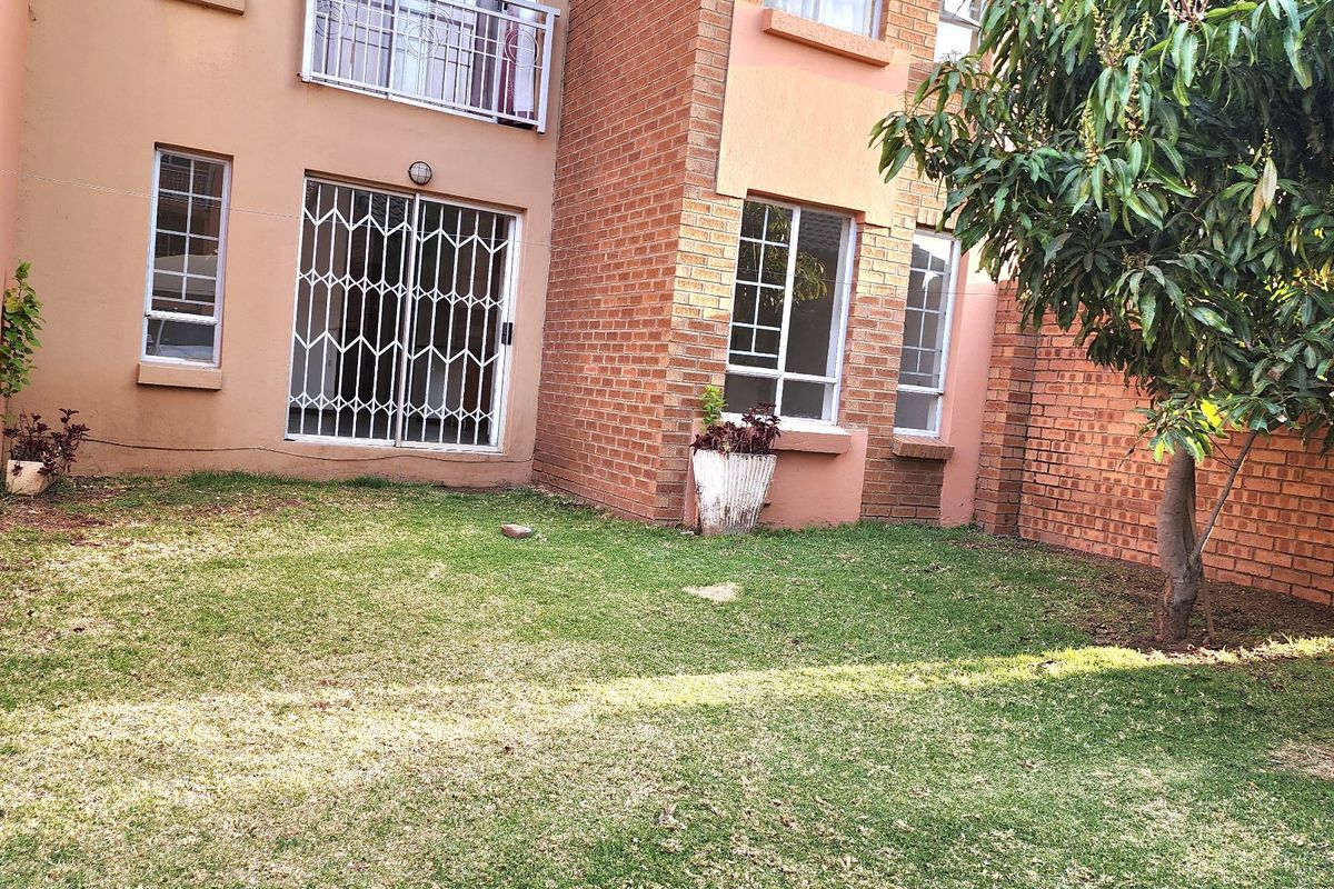 A private rear garden area featuring a brick facade, security-gated sliding door access, and established lawn space.