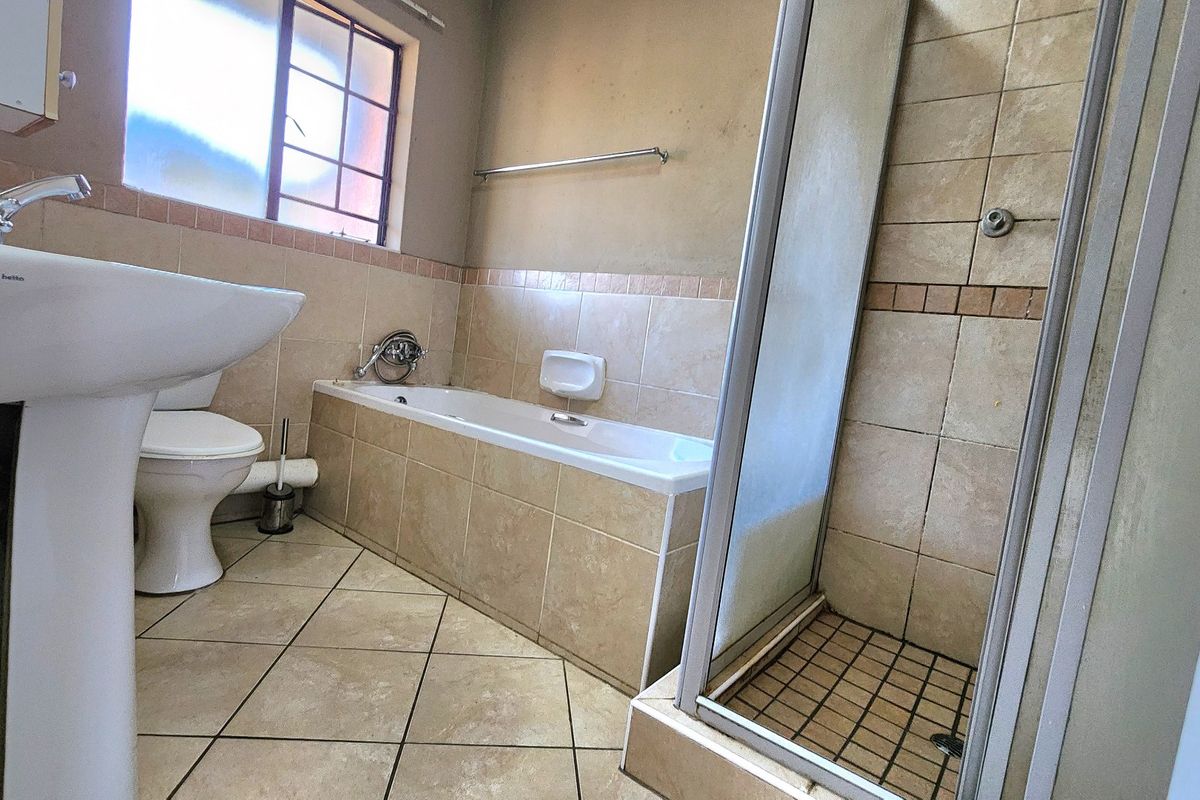 A functional bathroom featuring a pedestal basin, toilet, built-in bathtub, and a separate shower enclosure with tiled finishes throughout.