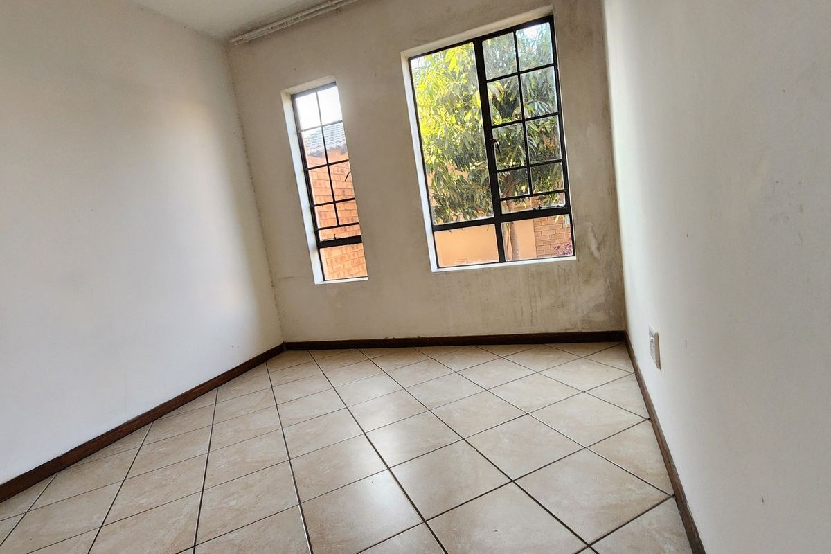 An empty bedroom featuring tiled flooring and steel-framed windows, showing signs of wall staining and plaster damage requiring maintenance.