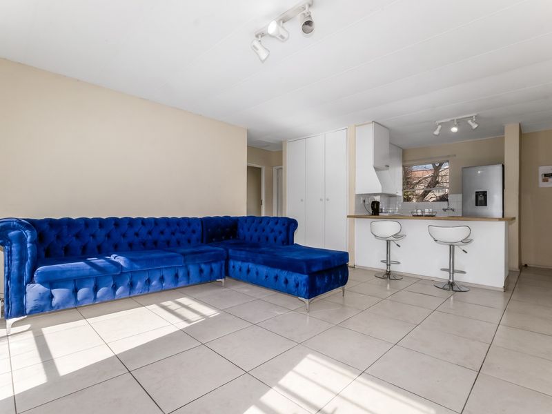 Open-plan living area featuring tiled flooring, track lighting, and a functional kitchen with a breakfast bar and built-in storage.