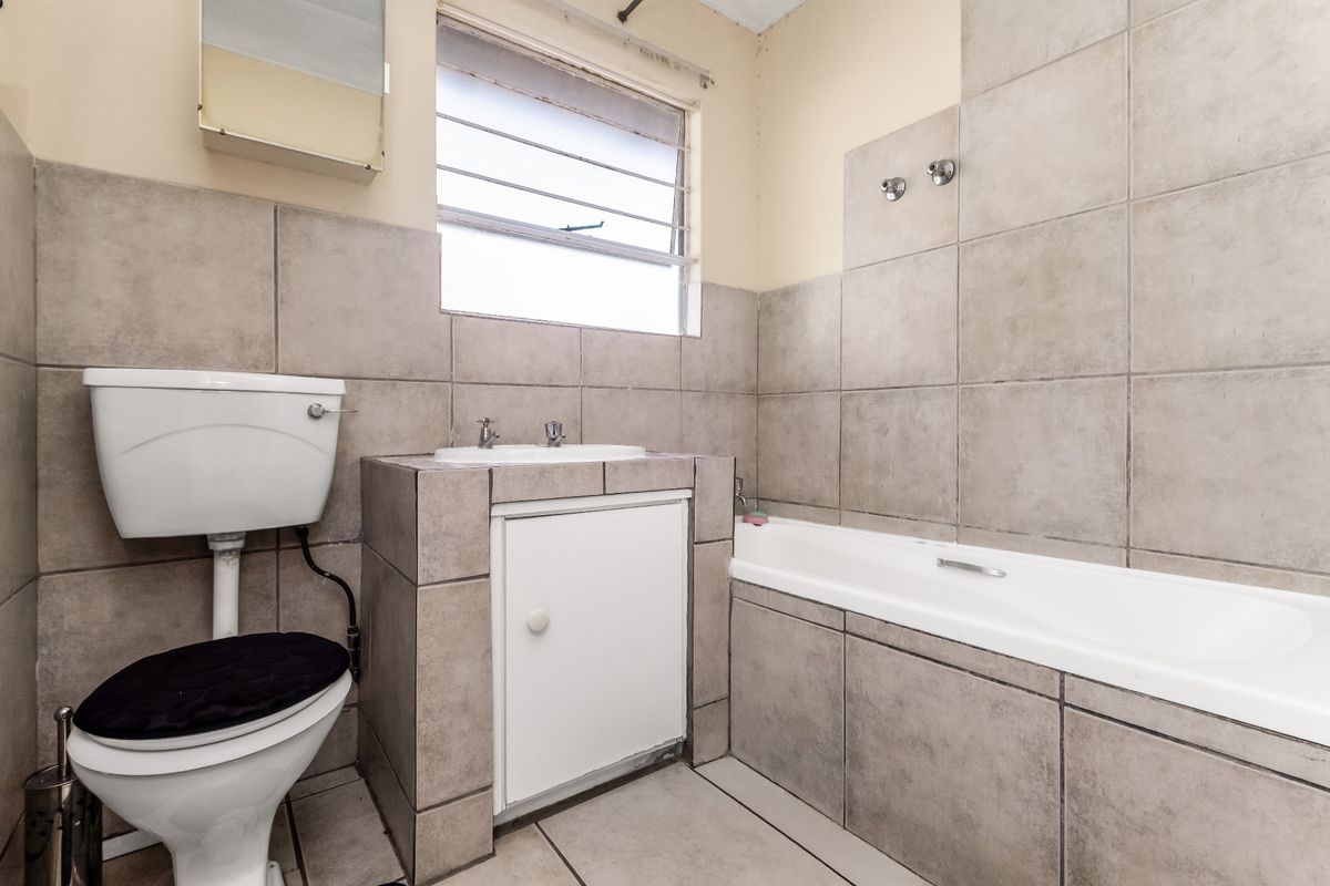 A functional bathroom featuring tiled walls and flooring, a built-in vanity with basin, a standard toilet, and a bathtub with shower plumbing.
