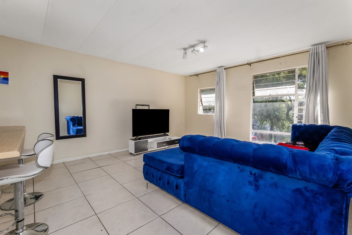 A bright living room featuring large windows, tiled flooring, and a ceiling-mounted spotlight track, offering a functional and open living space.