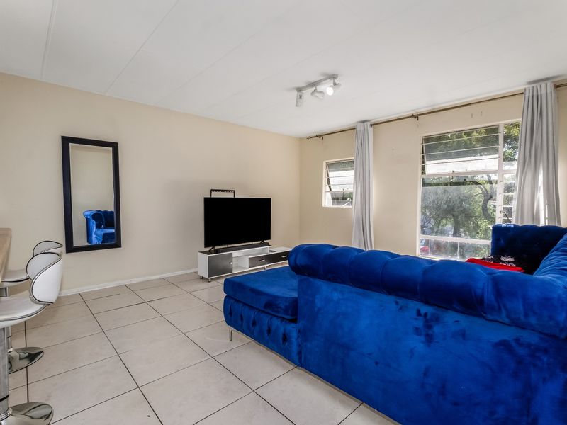 A bright living room featuring large windows, tiled flooring, and a ceiling-mounted spotlight track, offering a functional and open living space.