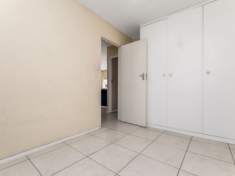 An empty bedroom featuring tiled flooring and a built-in white wardrobe, offering a neutral canvas for personalization.