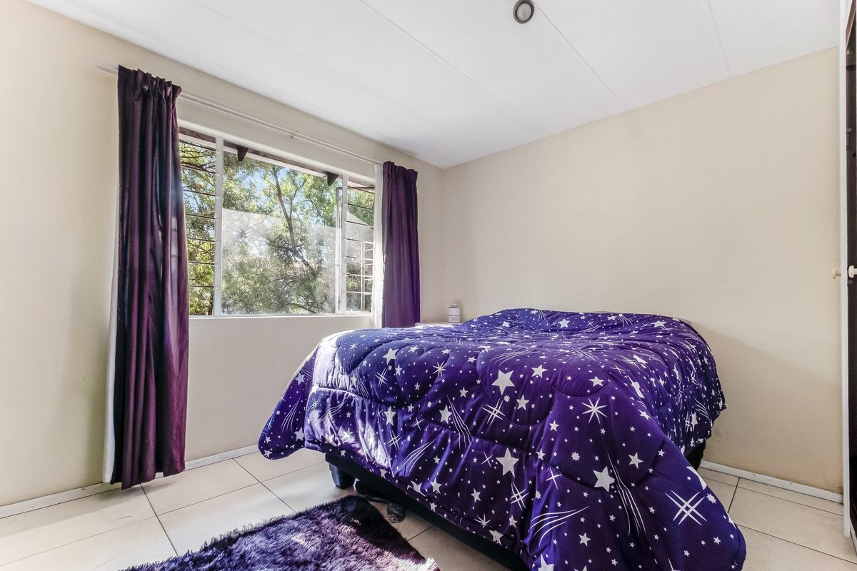 A functional bedroom featuring tiled flooring and a large window providing natural light and garden views.