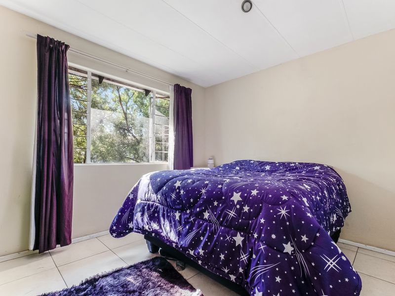 A functional bedroom featuring tiled flooring and a large window providing natural light and garden views.