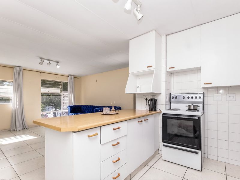 Open-plan kitchen and living area featuring white cabinetry, laminate countertops, a freestanding stove, tiled backsplash, and neutral tiled flooring throughout.