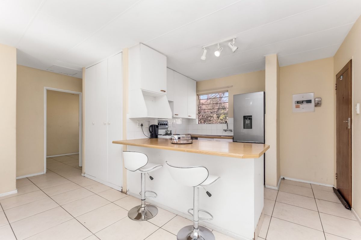 A functional kitchen featuring white cabinetry, a wooden breakfast bar, tiled flooring, and a tiled backsplash, offering a clean and practical layout.