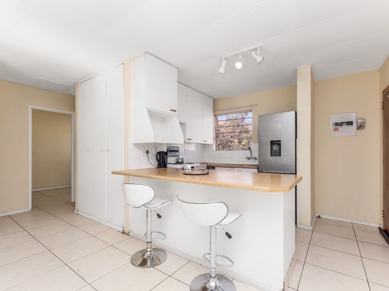 A functional kitchen featuring white cabinetry, a wooden breakfast bar, tiled flooring, and a tiled backsplash, offering a clean and practical layout.