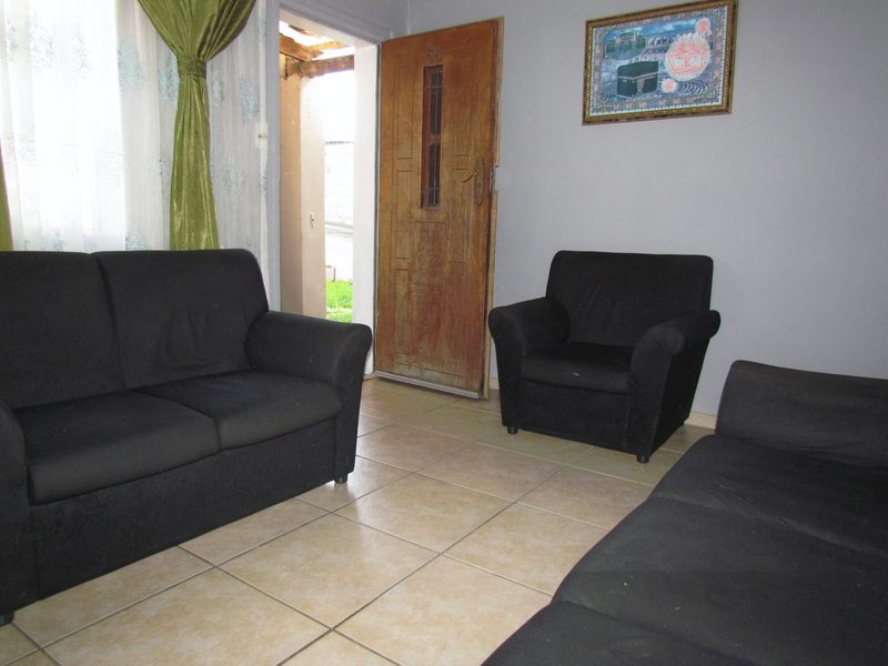 A living room area featuring tiled flooring and a wooden entrance door leading to the exterior.