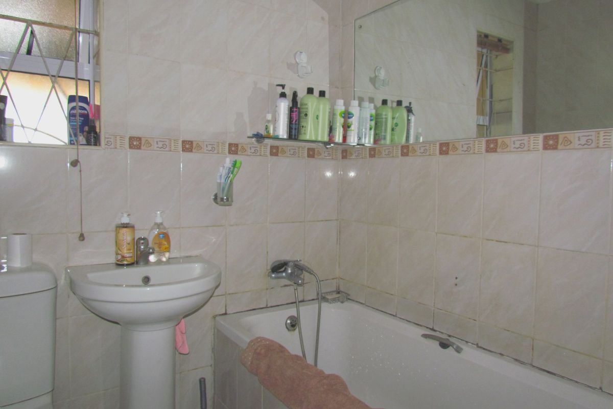 A dated bathroom featuring a pedestal basin, bathtub with wall-mounted mixer, and full-height ceramic wall tiling with a decorative border.