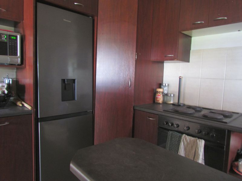 A functional kitchen featuring dark wood-finish cabinetry, a built-in oven with electric hob, and tiled splashbacks.