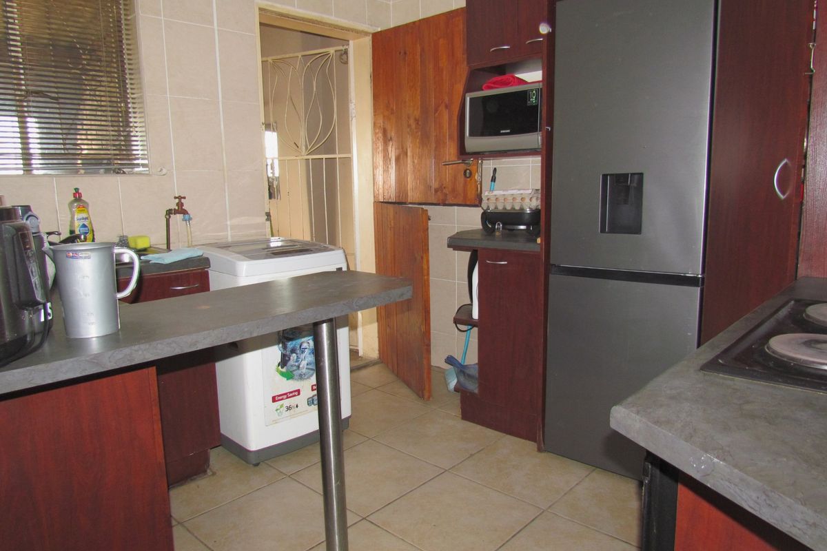 A functional kitchen featuring dark wood-look cabinetry, tiled surfaces, a breakfast bar, and direct access to an adjacent utility area.