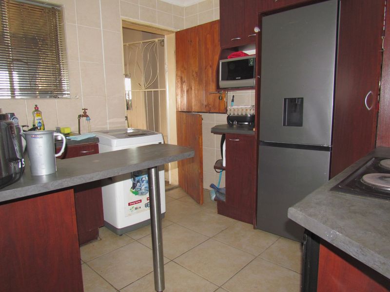 A functional kitchen featuring dark wood-look cabinetry, tiled surfaces, a breakfast bar, and direct access to an adjacent utility area.