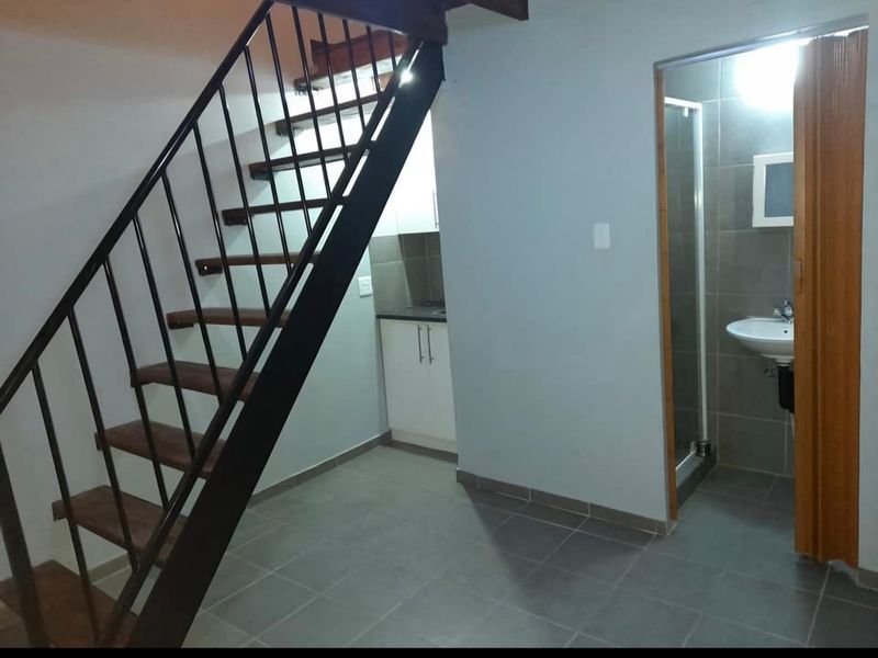 Open plan living area featuring a metal staircase, compact kitchen cabinetry, and an adjacent bathroom with a shower and pedestal basin.