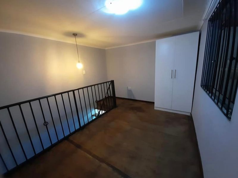An upper-level landing area featuring a built-in wardrobe, metal balustrade overlooking the stairs, and security bars on the window.