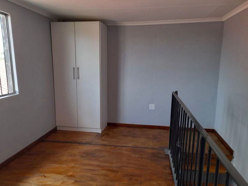 An empty bedroom featuring wooden flooring, a built-in wardrobe, and a metal staircase railing, offering a clean and functional space.