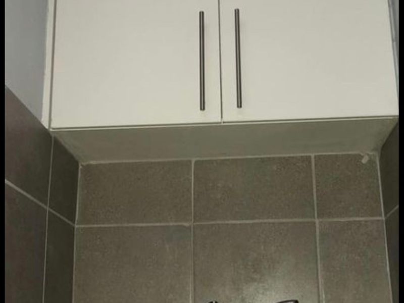 A functional laundry area featuring built-in white cabinetry, a stainless steel sink with a mixer tap, and neutral tiled splashback.
