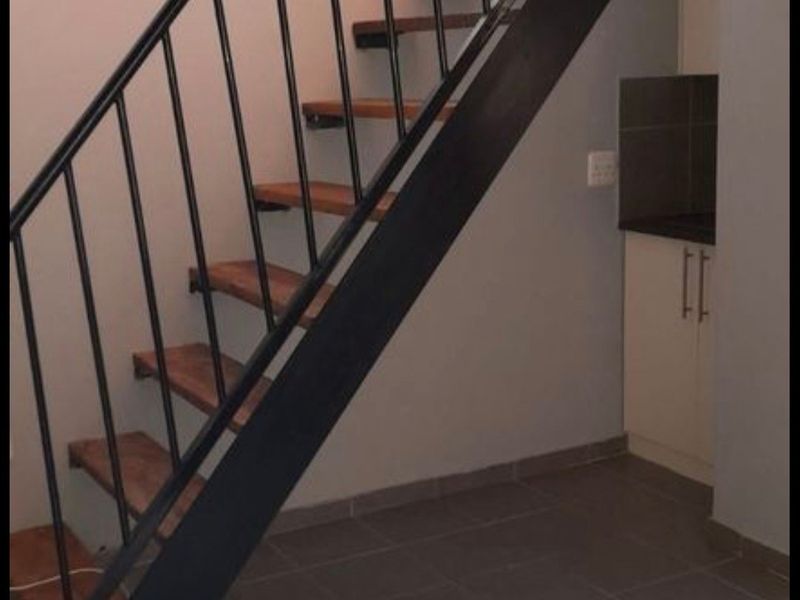 A functional hallway area featuring a modern staircase with a metal balustrade, tiled flooring, and a compact built-in storage unit.