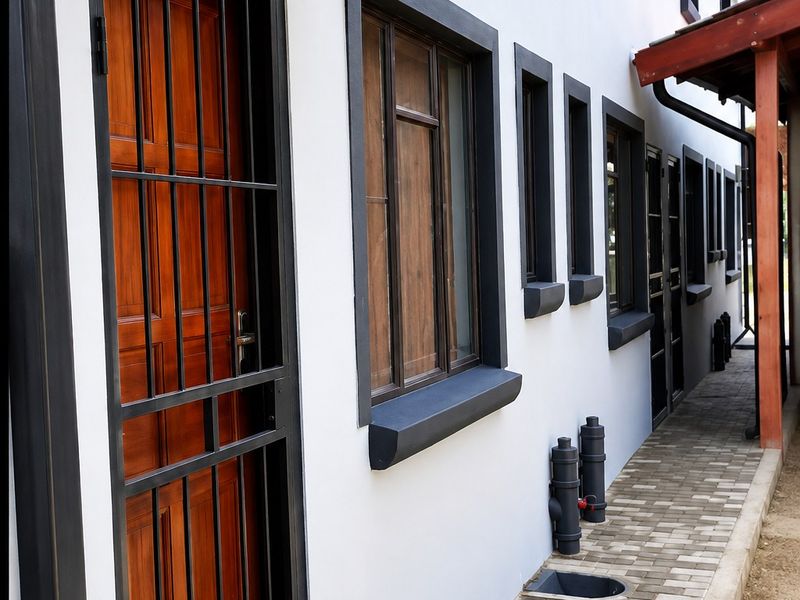 A well-maintained exterior rear walkway featuring a paved path, security gates, and modern window frames with a protective awning.