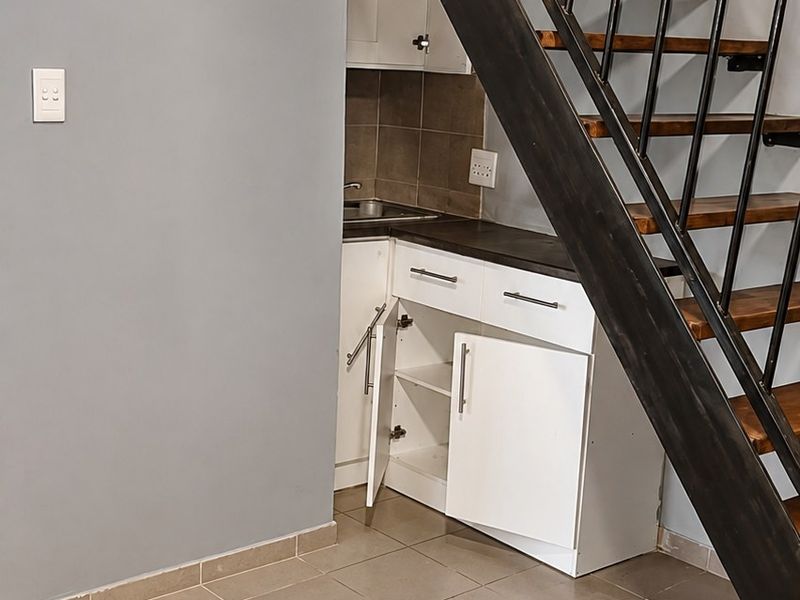 Compact kitchen area tucked under a staircase, featuring tiled flooring, built-in cabinetry, and exposed timber ceiling beams.