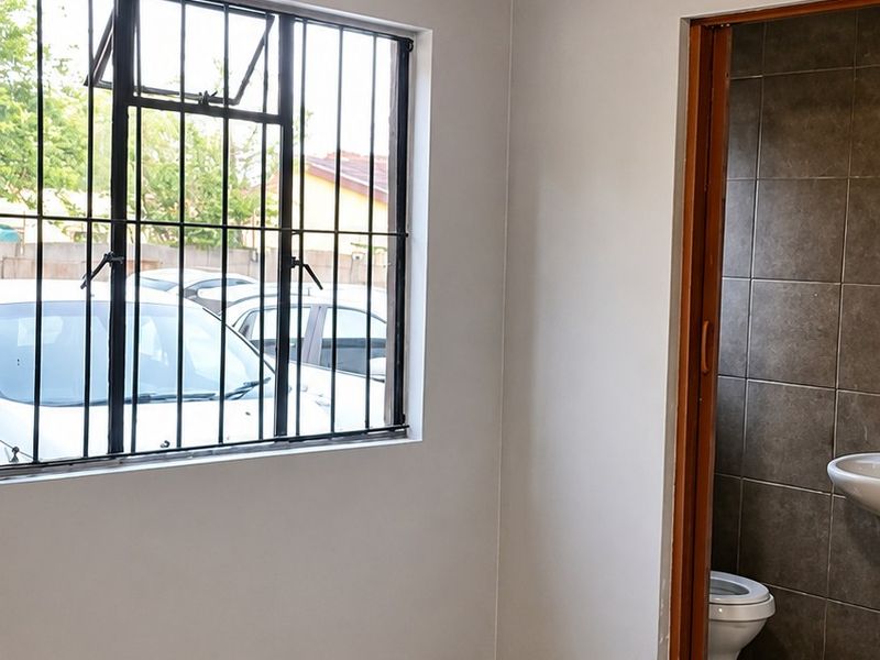An empty bedroom featuring exposed timber ceiling beams, tiled flooring, and an en-suite bathroom with a toilet and basin.