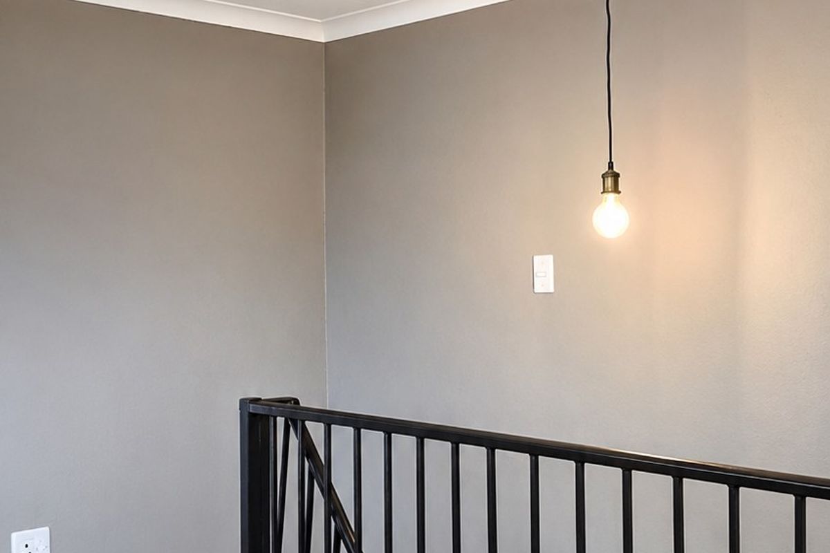 A clean, modern landing area featuring dark laminate flooring, a black metal balustrade, and a minimalist pendant light fixture.