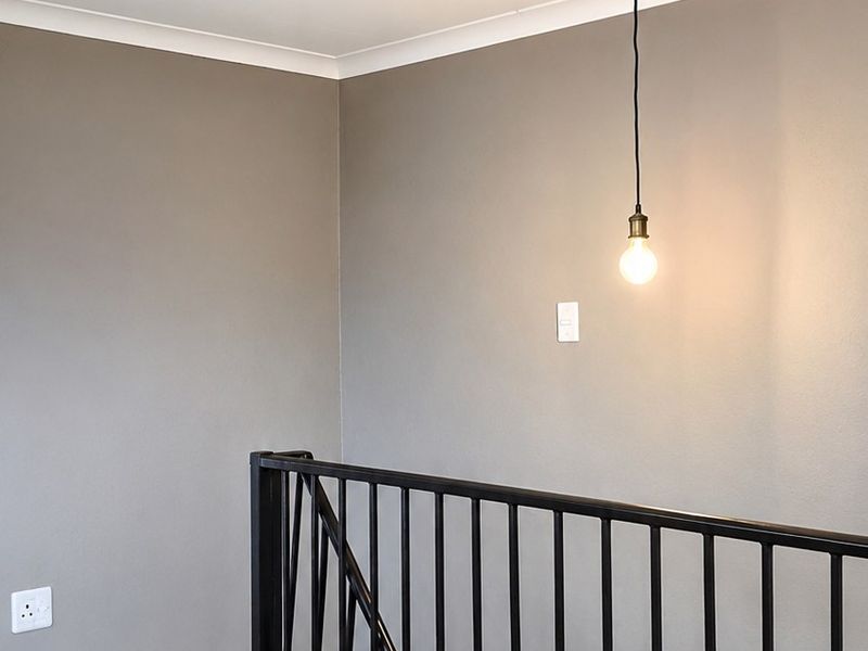 A clean, modern landing area featuring dark laminate flooring, a black metal balustrade, and a minimalist pendant light fixture.