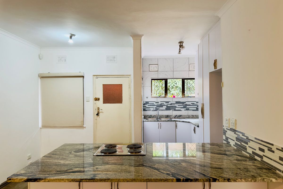 A clean, functional kitchen featuring a large granite-topped island with an integrated electric hob, ample built-in cabinetry, and a tiled backsplash.