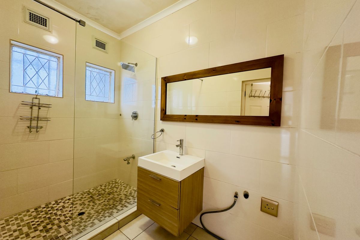 A functional bathroom featuring a walk-in shower with glass screen, wall-mounted vanity with basin, and neutral wall tiling.