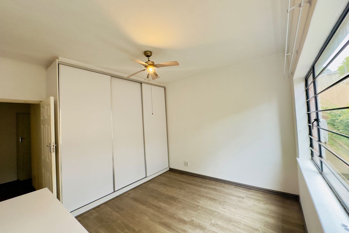 A bright, empty bedroom featuring laminate flooring, a large built-in wardrobe, and a ceiling fan.