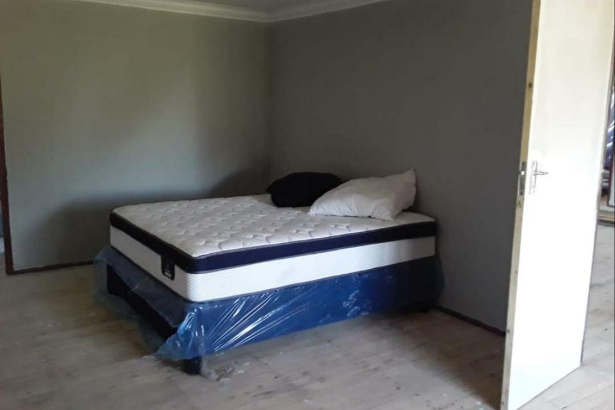 A sparsely furnished bedroom featuring timber flooring and neutral wall tones, currently requiring finishing touches to the flooring and door frames.