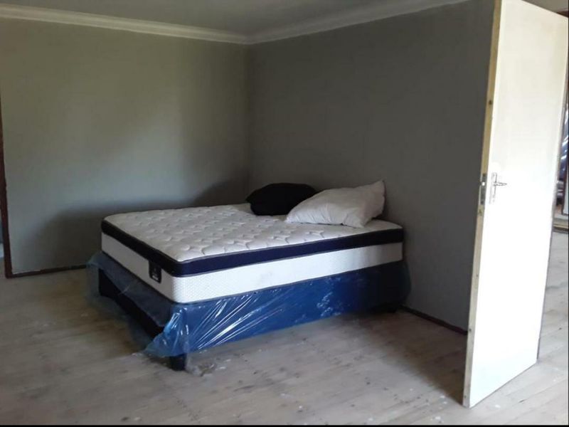 A sparsely furnished bedroom featuring timber flooring and neutral wall tones, currently requiring finishing touches to the flooring and door frames.