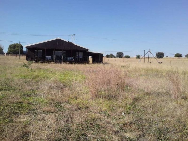 A detached timber-clad house featuring a covered deck and corrugated metal roof, situated on a large, undeveloped rural plot.