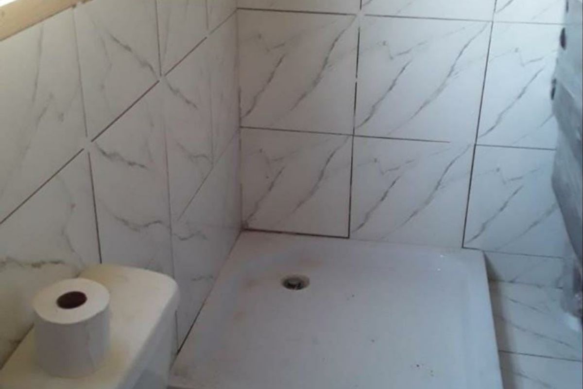 A compact bathroom featuring a shower tray, toilet, and marble-effect ceramic wall and floor tiling.