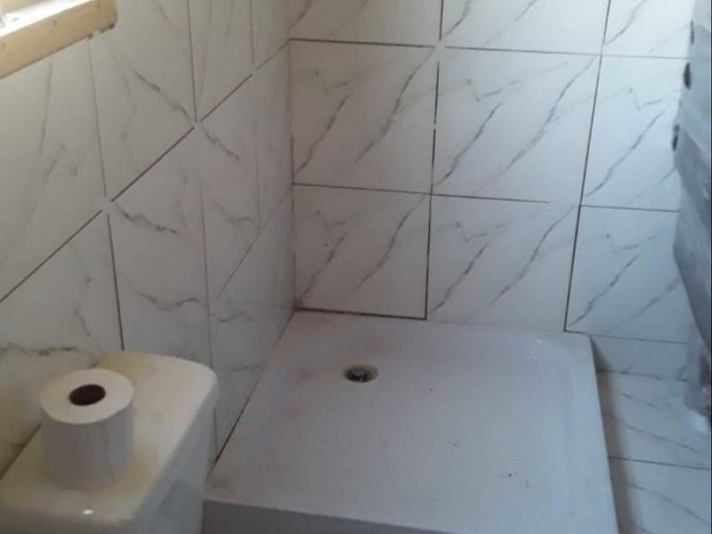 A compact bathroom featuring a shower tray, toilet, and marble-effect ceramic wall and floor tiling.