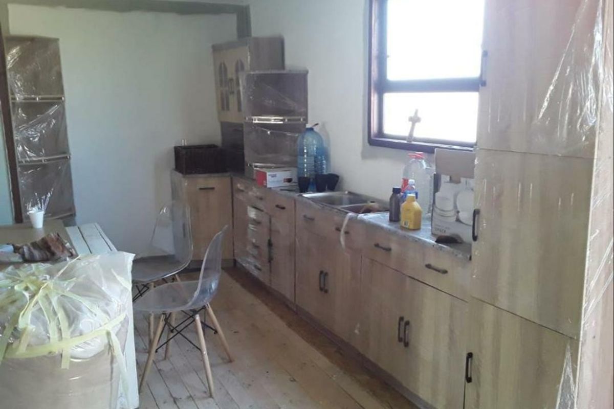 A kitchen area featuring light wood-finish cabinetry and a stainless steel sink, currently undergoing renovation with unfinished walls and flooring.