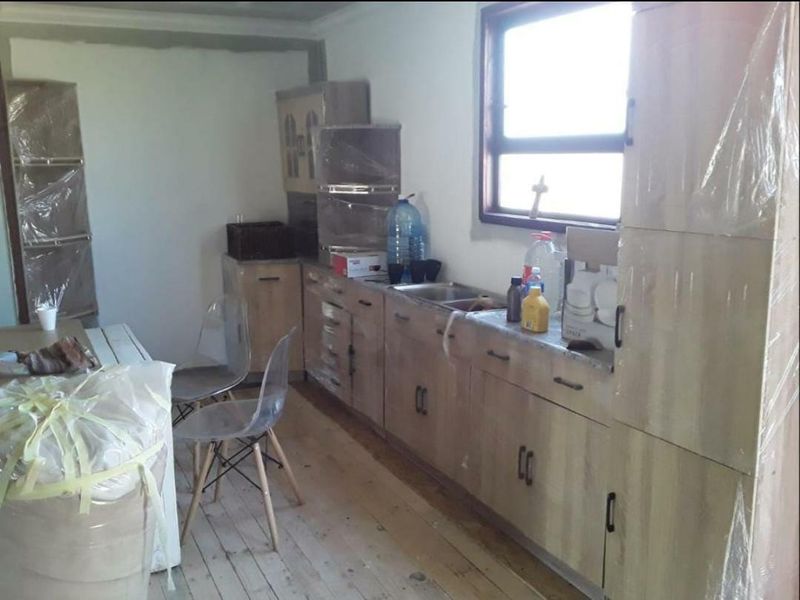 A kitchen area featuring light wood-finish cabinetry and a stainless steel sink, currently undergoing renovation with unfinished walls and flooring.