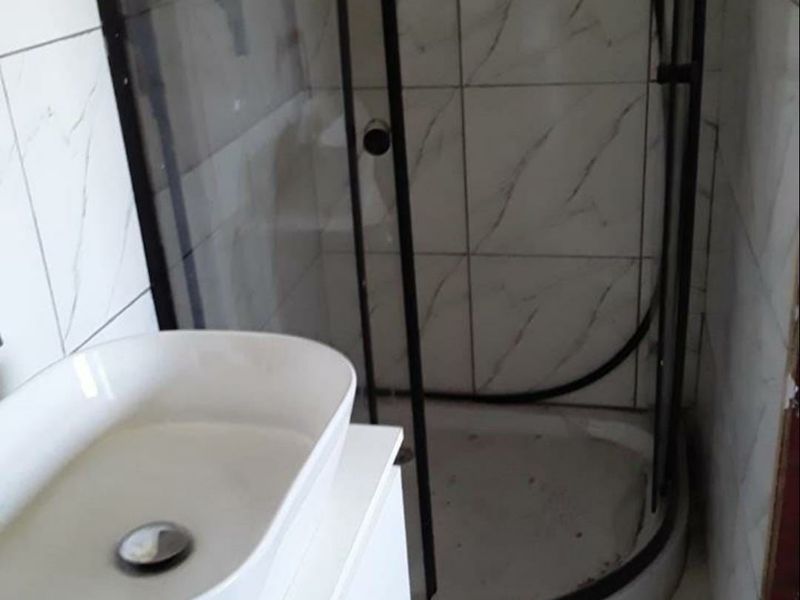 A compact bathroom featuring a corner shower enclosure with black framing and a modern vanity basin with tiled finishes throughout.
