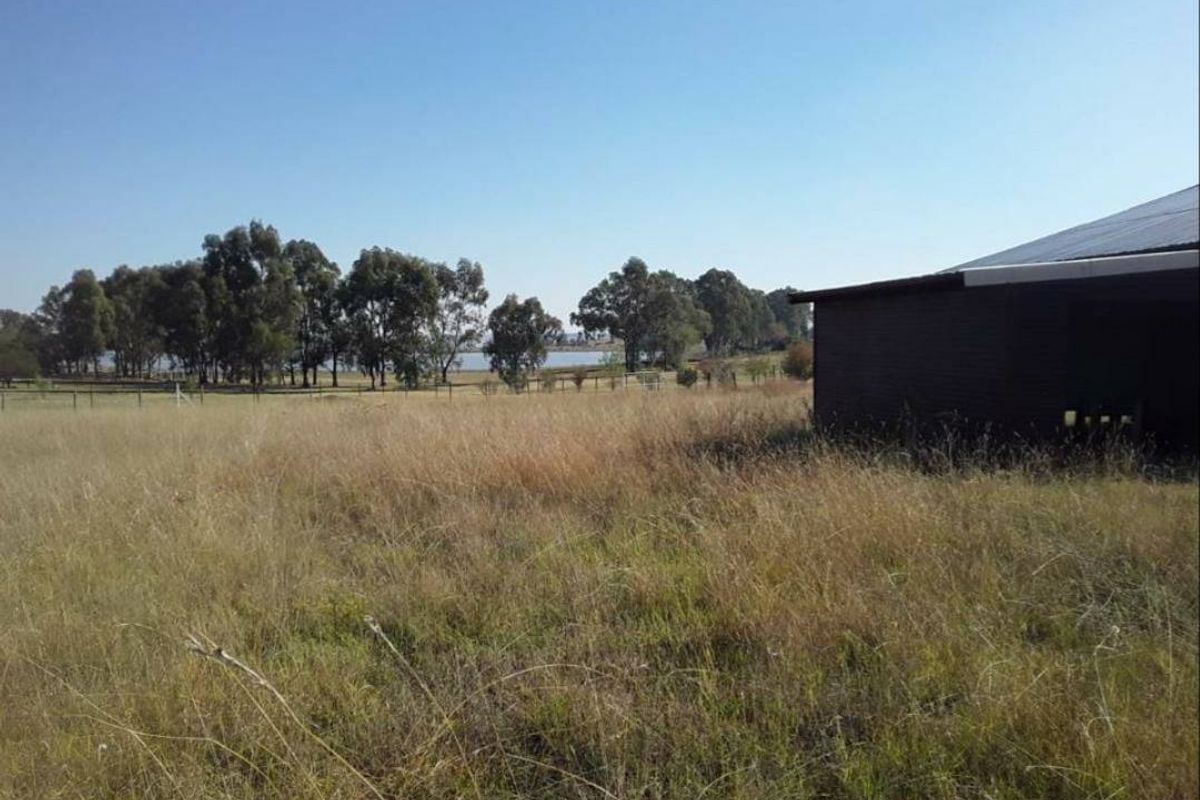 Expansive rural land featuring a large outbuilding with a corrugated metal roof and scenic views of surrounding trees and water.