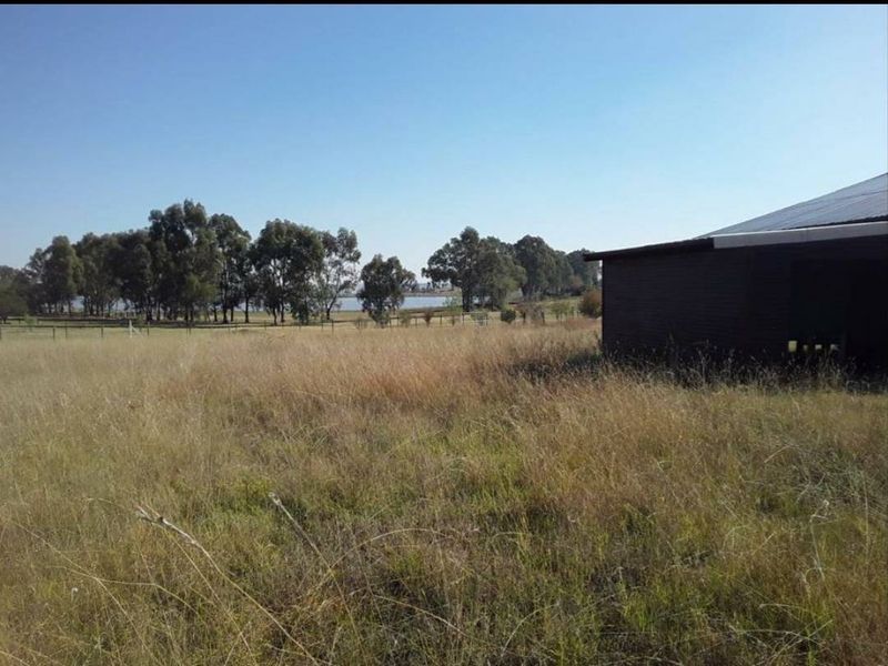 Expansive rural land featuring a large outbuilding with a corrugated metal roof and scenic views of surrounding trees and water.