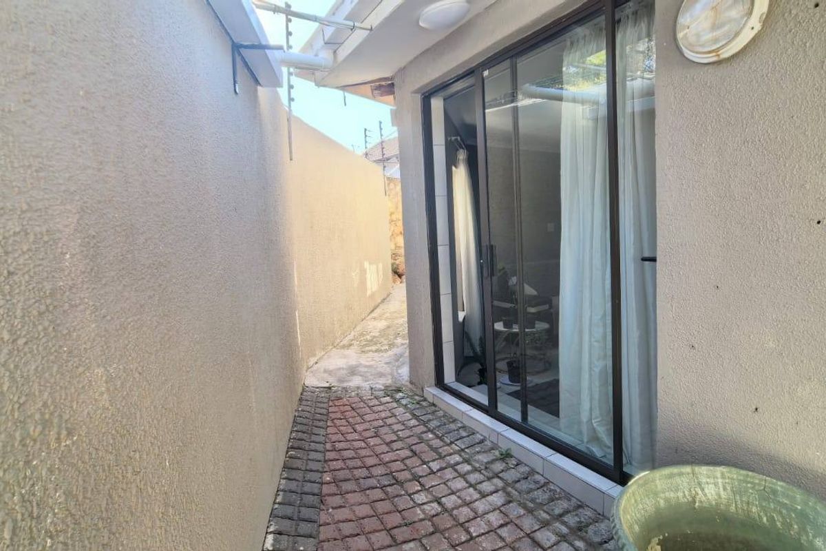 A narrow side passage featuring a paved walkway, boundary wall with electric fencing, and a sliding glass door providing access to the interior.