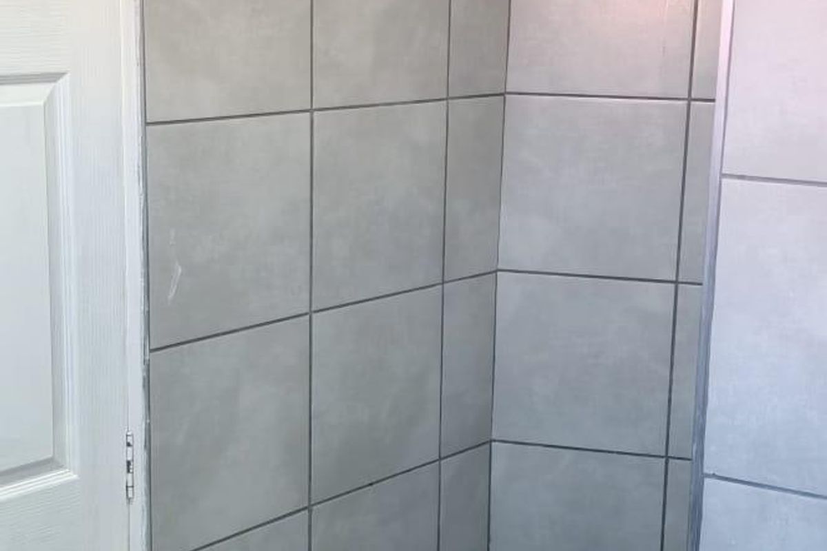 A clean, tiled shower enclosure featuring a built-in step and a wall-mounted towel rail.