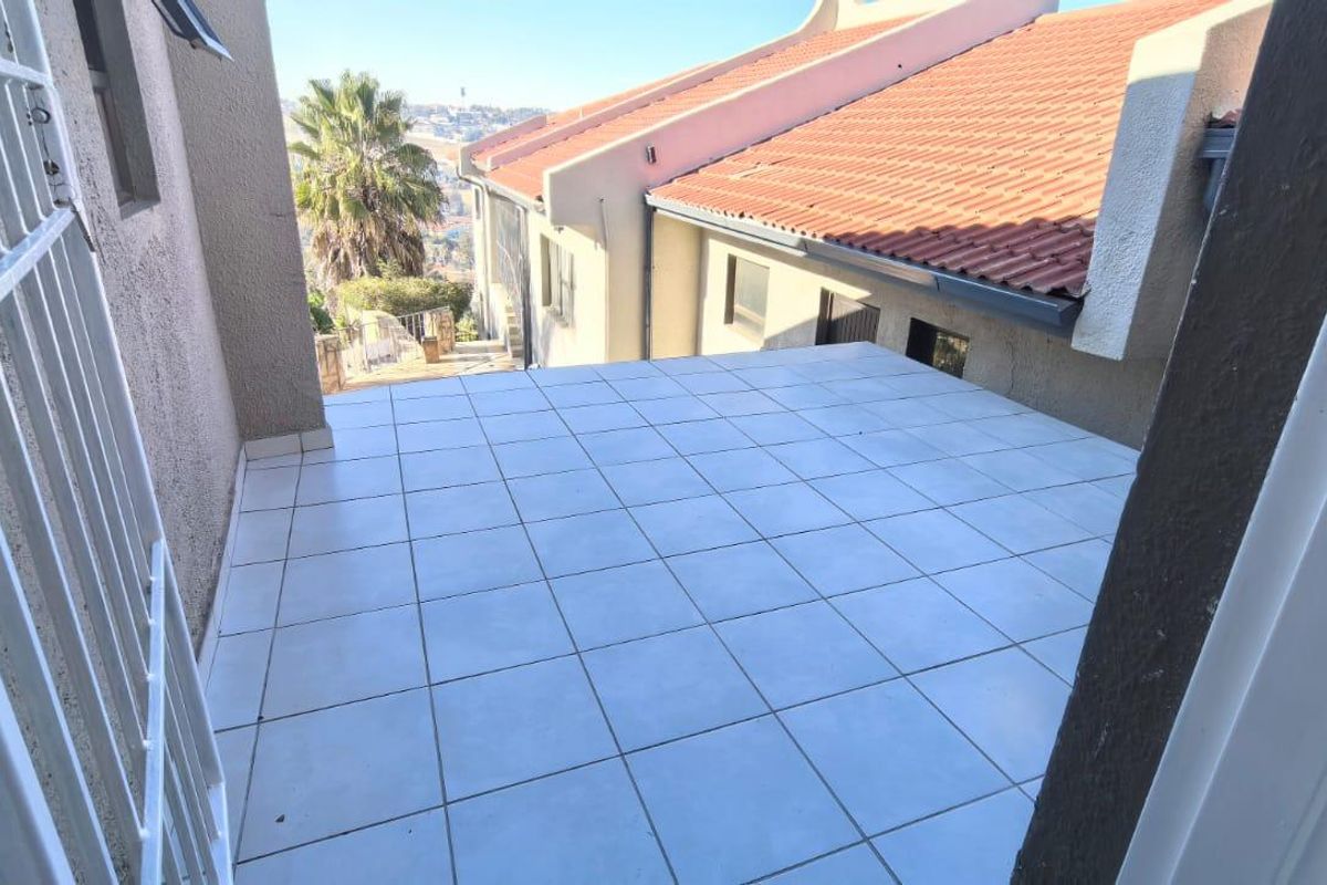 An open-air balcony featuring tiled flooring and a security gate, offering an elevated view of the surrounding residential area.