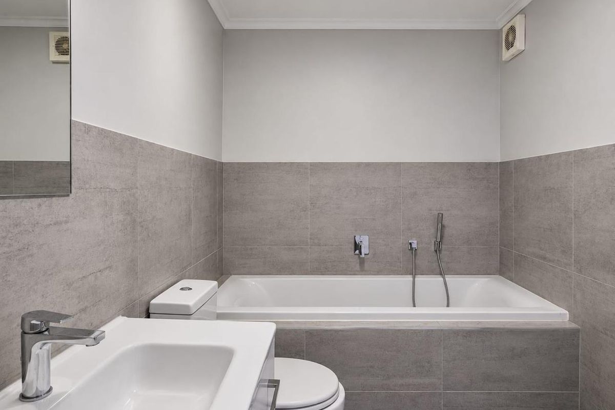 Modern bathroom featuring a built-in bathtub with handheld shower, vanity basin, toilet, and neutral grey wall tiling.
