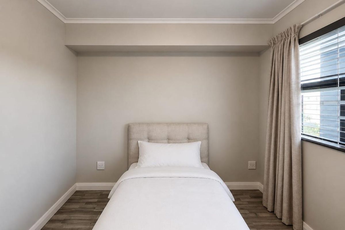 A clean and well-maintained bedroom featuring neutral wall tones, laminate flooring, and a window with fitted blinds.