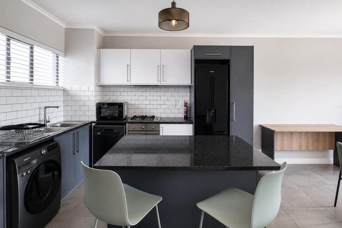 Modern kitchen featuring dark cabinetry, granite countertops, subway tile backsplash, and a central island with integrated appliances and contemporary pendant lighting.